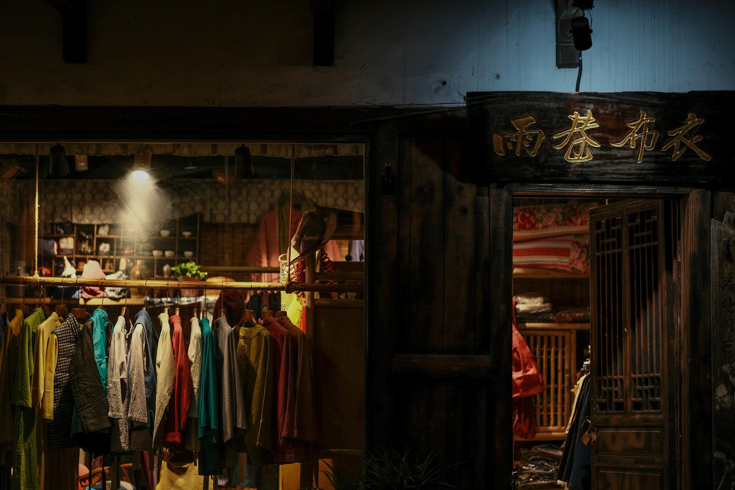 Traditional clothing store facade with colorful garments and Chinese characters in dim lighting.